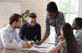 Vijf mensen aan tafel overleggen met elkaar aan de hand van een notitie