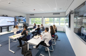 Een onderwijslokaal met een paar studentne die fysiek aanwezig zijn en een student die online onderwijs volgt