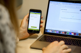 Persoon achter een computer is aan het inloggen met behulp van een app op een mobiele telefoon