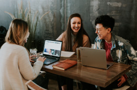 drie studenten zitten met laptop lachend aan tafel