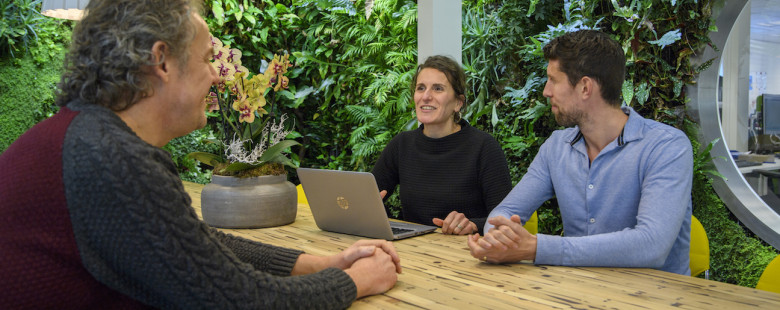 Drie mensen vergaderen rondom een tafel