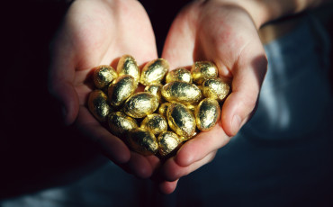 Two hands holding golden chocolate Easter eggs