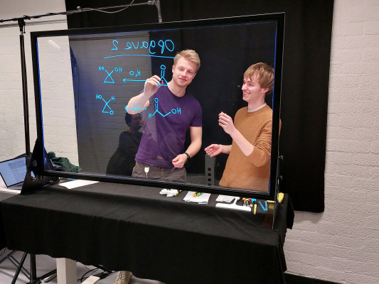 Thomas Hansen en Jaap Harteveld staan voor een zwarte achtergrond en schrijven op het Lightboard