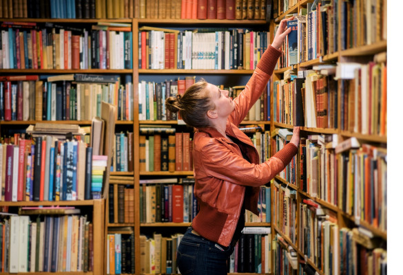 Iemand reikt naar een boek in een boekenkast