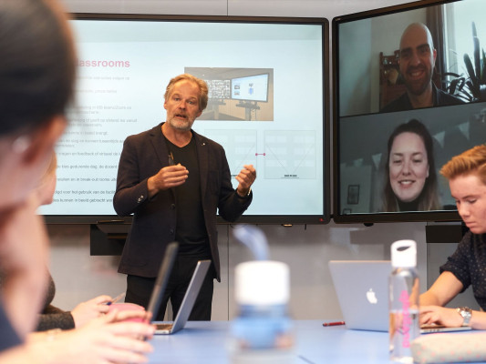 Docent voor de klas met een scherm met studenten die online aanwezig zijn. 