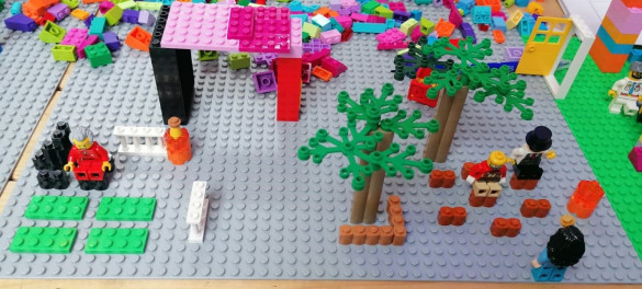 Een LEGO-bouwwerk met bomen, overkapping, zitplaatsen en poppetjes