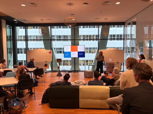 sessieruimte met banken, whiteboards en een aantal deelnemers aan de sessie. 