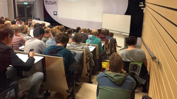 Een volle collegezaal met zelfs studenten op de trappen