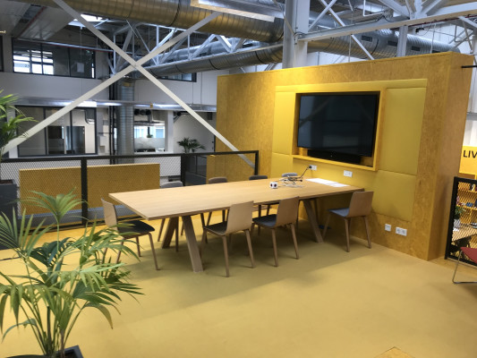 Ruimte met tafels en stoelen en groot TV scherm en een plant