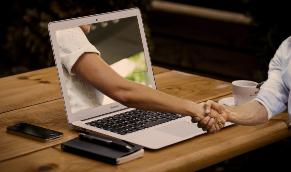Online ontmoeten: een digitale arm die uit een laptop komt en een echte arm een hand geeft.