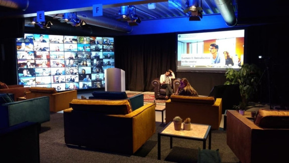 Een hybrid virtual onderwijslokaal met studenten op afstand van elkaar en een groot scherm met daarop de online studenten