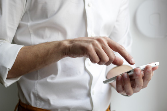 ingezoomd: man met witte blouse toetst met zijn rechterhand op zijn mobiele telefoon 