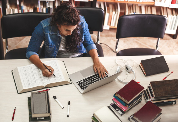 meisje zit aan het bureau met laptop en studieboeken