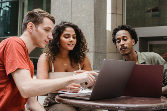 drie jongeren aan een ronde tafel waarop twee laptops staan