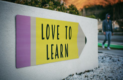 op een muur staat een bord in de vorm van een potlood met daarop de tekst: love to learn