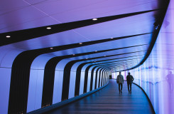 twee mensen lopen in een futuristische tunnel met paars en blauw licht