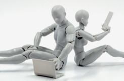 Twee plastic robots met menselijke gestalte met laptop en tablet zitten op vloer.