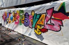 Comeniusfestival geschreven in graffiti, met spuitbussen op voorgrond