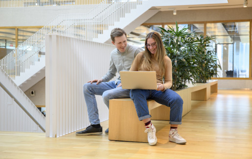 Twee studenten in een open hal met een laptop